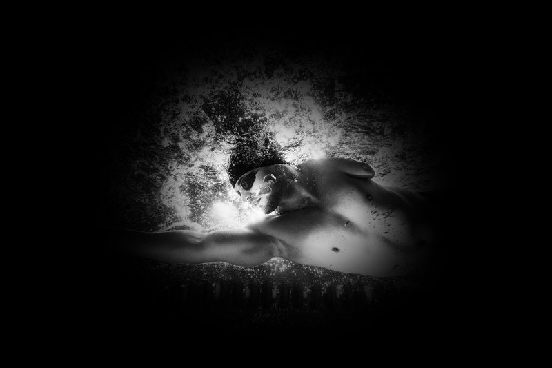 Moški, fotografiran od spodaj, se prebija skozi bazen. Celoten prizor ob robovih zakriva tunelska tema, ki ponazarja, kako bi ta prizor videl človek s pigmentno retinopatijo.